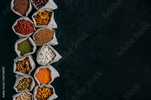 Photo of healthy food ingredients in little sacks, isolated over black background with empty space for your promotion. Bags of cereals and beans, fruit in one row