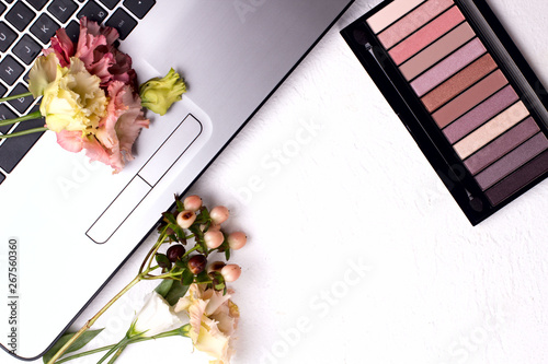 Laptop with flowers and cosmetics on white table. Freelancer workspace.