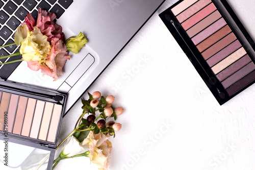 Laptop with flowers and cosmetics on white table. Freelancer workspace.