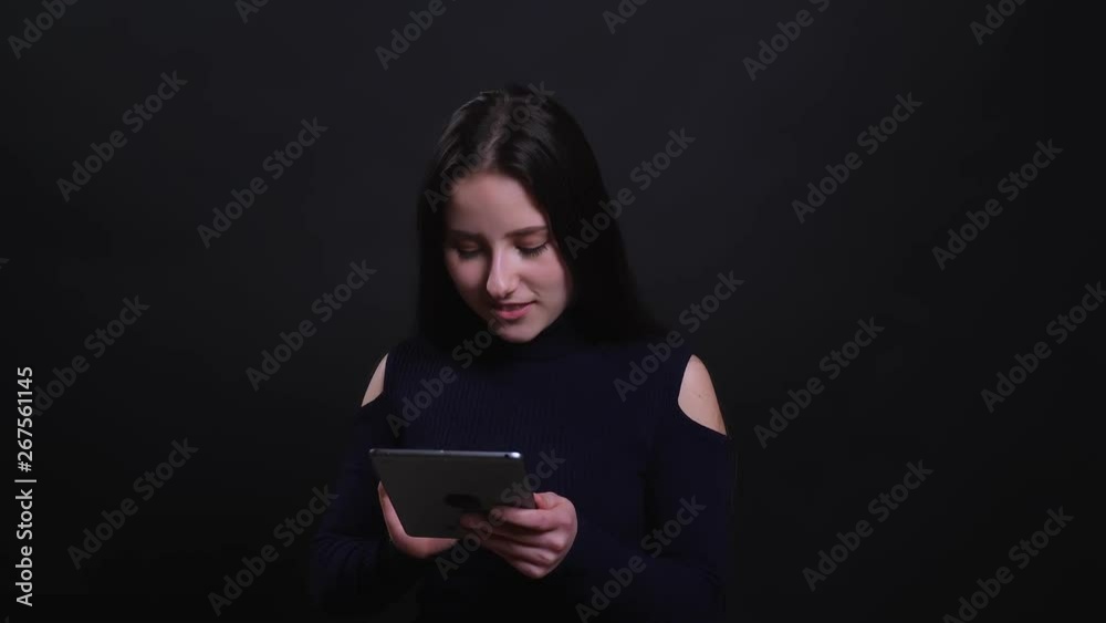 Closeup portrait of young attractive brunette female using the tablet with background isolated on black Closeup portrait of young attractive brunette female using the tablet with background isolated on black