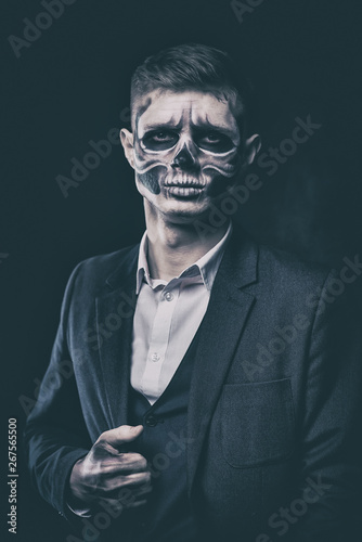 Stylish and beautiful, emotional young man with skeleton makeup in a strict suit against the background of smoke and dark background to Halloween