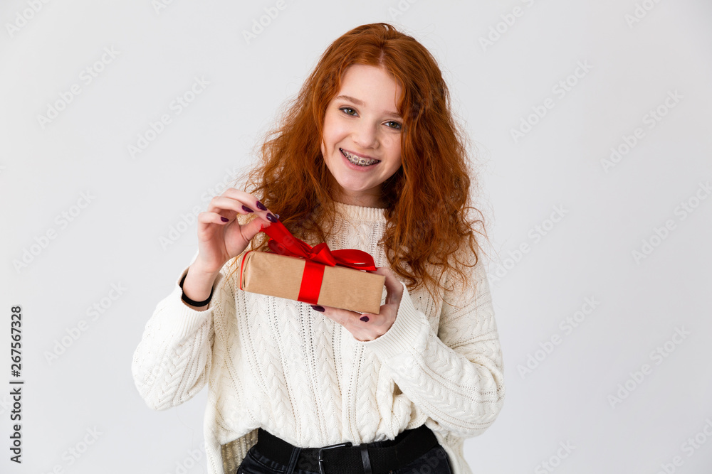 Beautiful young cute girl redhead posing isolated over white wall background holding gift box. Beautiful young cute girl redhead posing isolated over white wall background holding gift box.