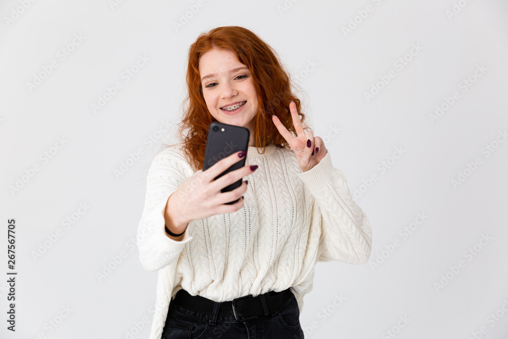 Beautiful young girl redhead posing isolated over white wall background take a selfie. Beautiful young girl redhead posing isolated over white wall background take a selfie.