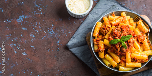 Cuadro en lienzo Delicious rigatoni pasta with italian tomato meat ragu sauce served in a pan on dark brown background