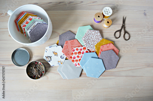 Hexagon english paper piecing templates, white cup, thread, retro scissors and metal pins on the wooden table