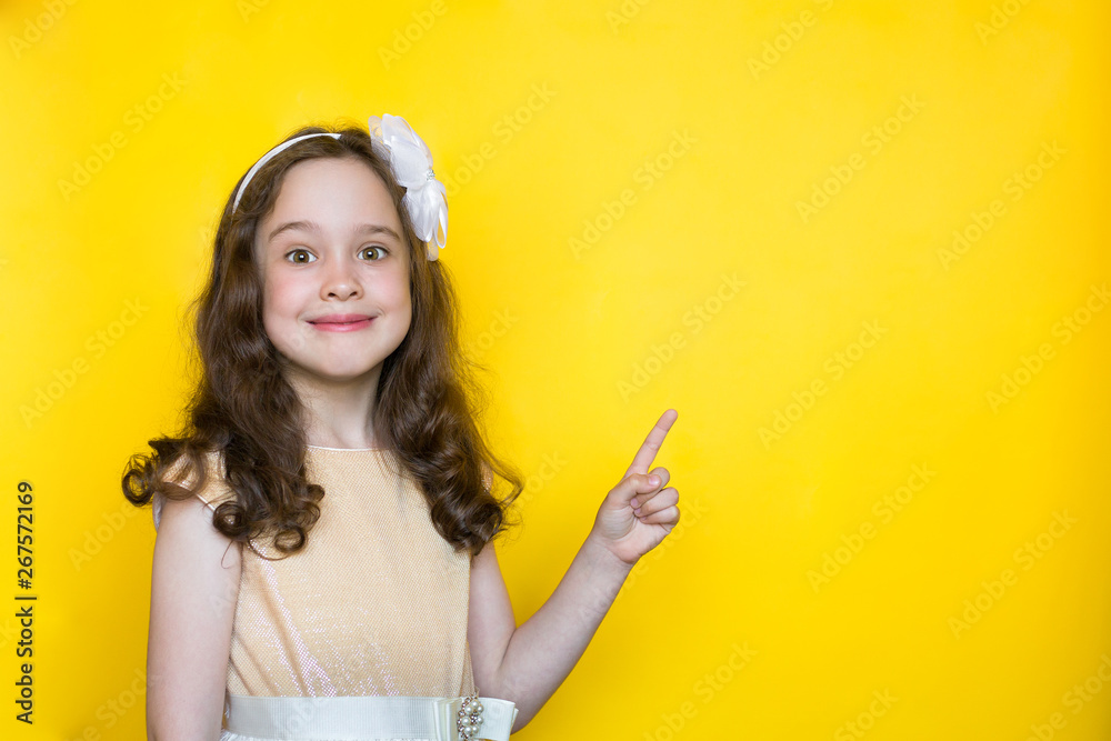 happy little girl on yellow background points her finger at the space for lettering. Concept of education happy little girl on yellow background points her finger at the space for lettering. Concept of education