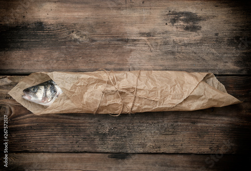 Canvas Print Fresh whole sea bass fish wrapped in a brown paper