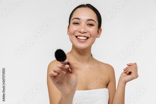 Pretty asian woman with healthy skin posing naked isolated over white wall background holding makeup brush.