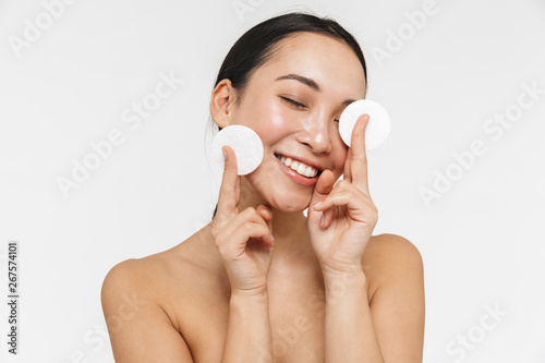 Beautiful young pretty asian woman with healthy skin posing naked isolated over white wall background holding cotton pads.