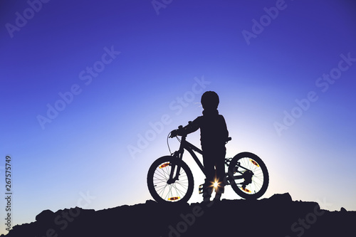 Silhouette of a little girl with a bicycle at sunset