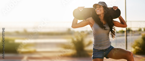Smiling woman holding skateboard during sunse in panoramic composition