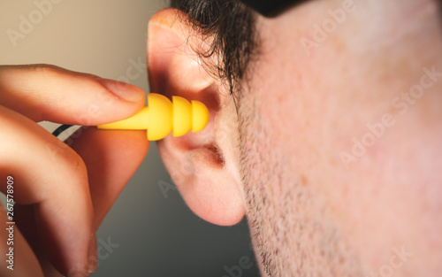 Foto Man worker inserting yellow hearing safety protection earplug in his ear close u