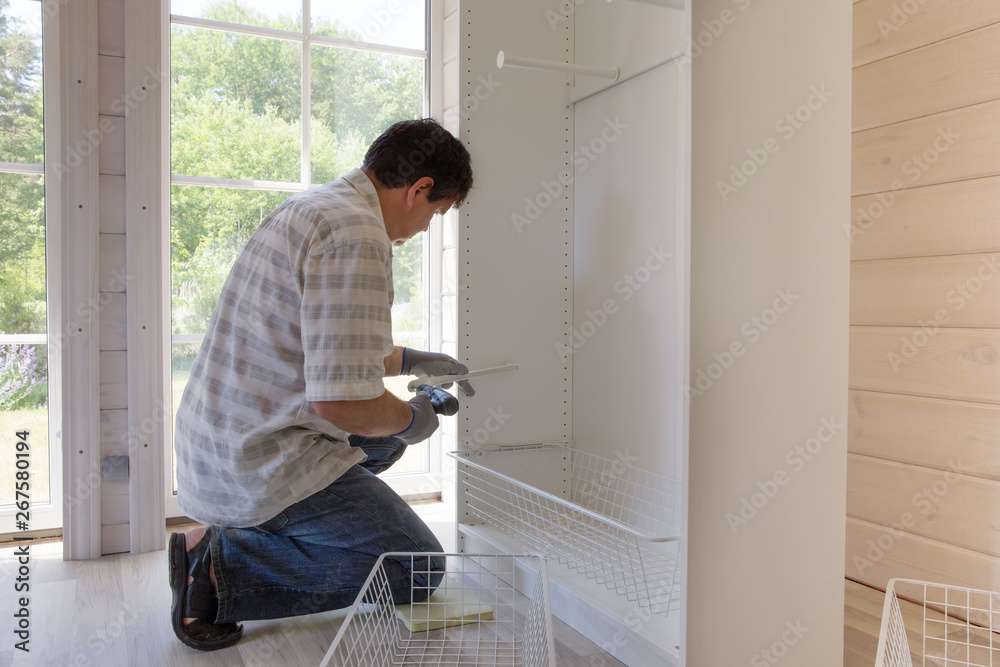 The process of assembling furniture, the master assembles a white cabinet using an electric drill The process of assembling furniture, the master assembles a white cabinet using an electric drill