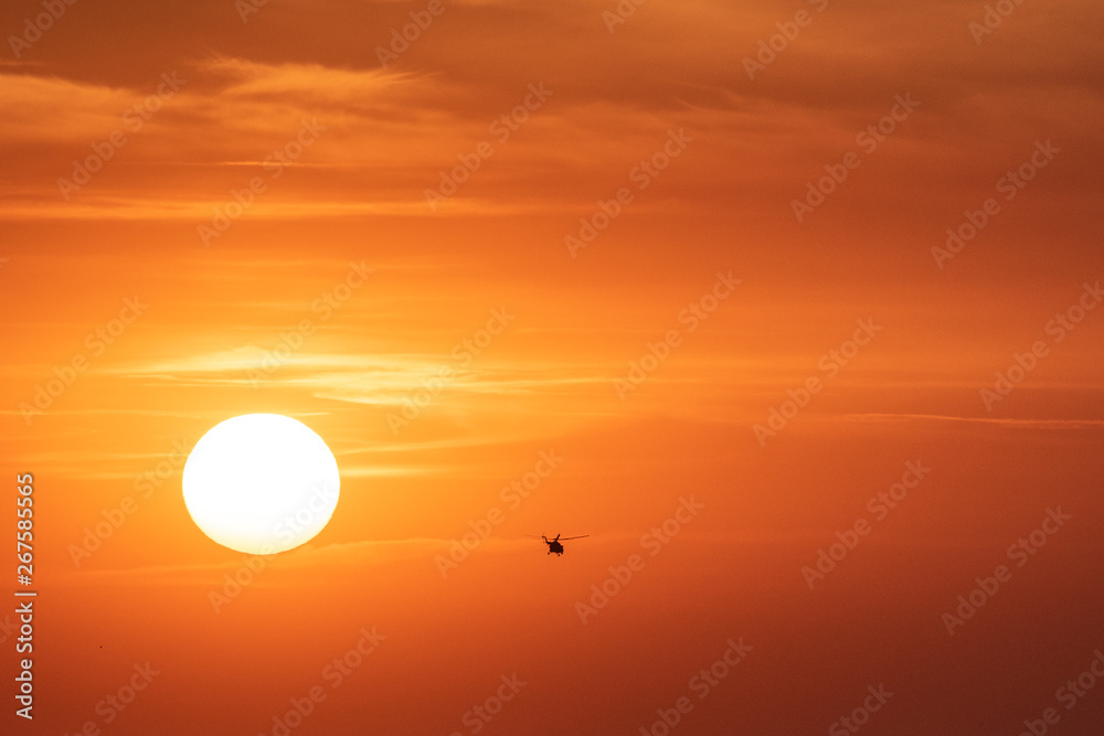 Sunset orange sky background at evening with clouds and silhouette of the helicopter Sunset orange sky background at evening with clouds and silhouette of the helicopter