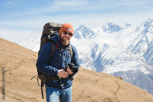 Portrait of smiling bearded male photographer in sunglasses against the background of snow-capped mountains on a sunny day © yanik88