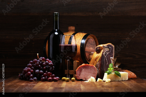 Fototapeta Naklejka Na Ścianę i Meble -  Still life in a rustic style. Grapes on a wooden table with a bottle of wine and meat and cheese. Antipasto and red wine