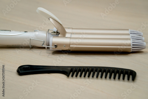 Brown hair straightener with black comb on the wooden background. Hair care