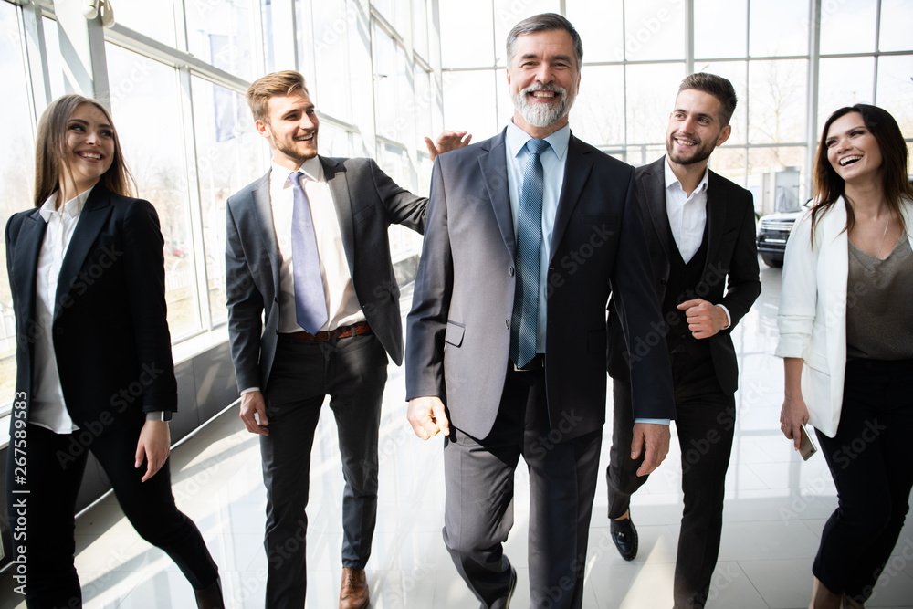 Business People Team Walking In Modern Office, Confident Businessmen And Businesswomen In Suits Diverse With Mature Leader In Foreground. Business People Team Walking In Modern Office, Confident Businessmen And Businesswomen In Suits Diverse With Mature Leader In Foreground.