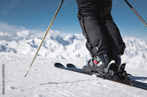 Close-up of the athlete's skier's foot in ski boots rises into the skis against the background of the snow-capped Caucasus mountains on a sunny day. Winter sports concept