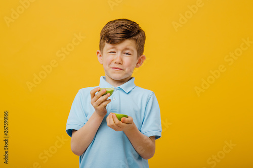 beautiful boy taste a fresh lime taste sour grimace, facial emotions negative, in blue T-shirt, isolated yellow background, copy space photo