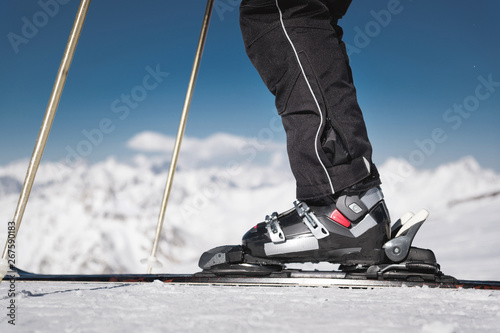 Close-up of the athlete's skier's foot in ski boots rises into the skis against the background of the snow-capped Caucasus mountains on a sunny day. Winter sports concept photo
