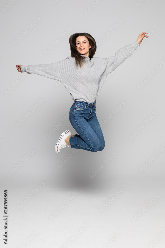 Full length portrait of a laughing woman jumping over gray background.