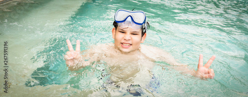 Happy teen boy in the swimming pool at aquapark. Cute child having fun enjoyable time on vacation.