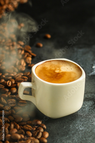 coffee in a white cup and coffee grain scattered on the table (freshly brewed hot drink with foam). food background. top