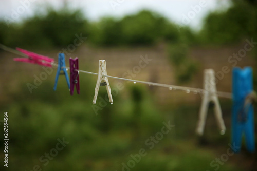 Wet colorful pegs hanging on a clothesline after the rain in the backyard. No clothes outside, it’s time to use dryer.