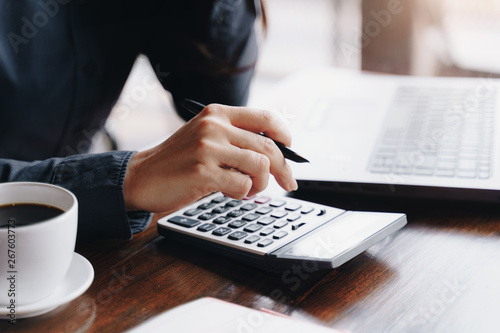 Woman entrepreneur using a calculator to calculating financial expense at coffee shop.