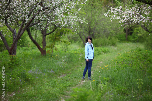 Beautiful mature woman posing for the camera in the spring garden. The girl enjoys the flowering of apple trees.