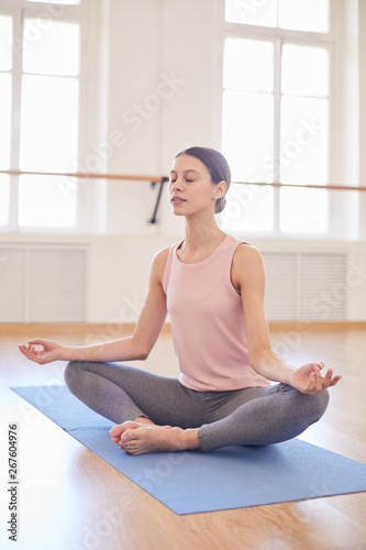 Calm serene girl with hair bun concentrated on meditation sitting in butterfly pose and keeping eyes closed at yoga class