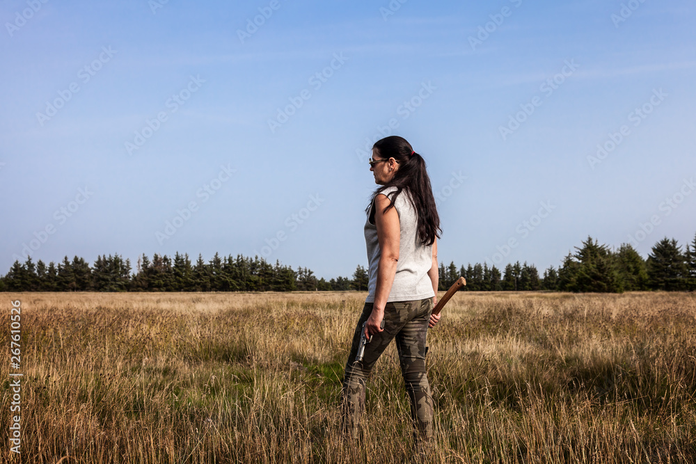 Attraktive Frau mit Pistole und Axt auf einem Feld schaut in die Ferne