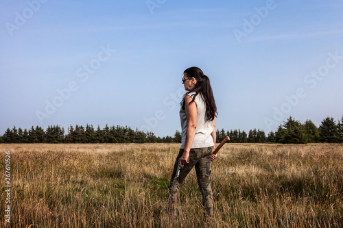 Attraktive Frau mit Pistole und Axt auf einem Feld schaut in die Ferne