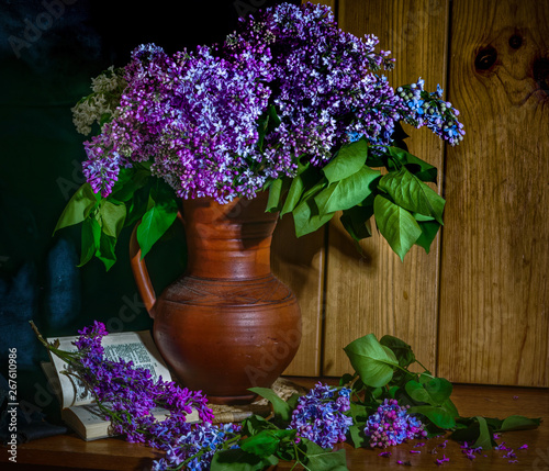Lilac in a ceramic vase, a book and an hour on the table
