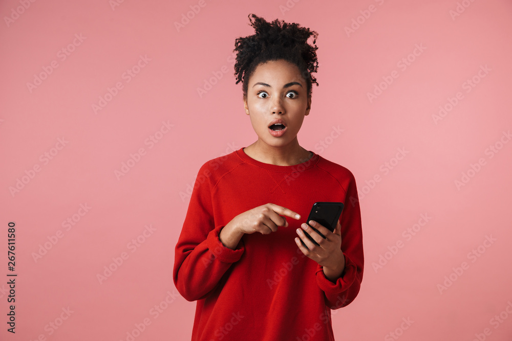 Shocked excited young african woman posing isolated over pink wall background using mobile phone. Shocked excited young african woman posing isolated over pink wall background using mobile phone.