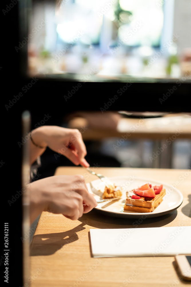 Girl eating waffle dessert with berries on a wooden table in a cozy cafe restaurant.