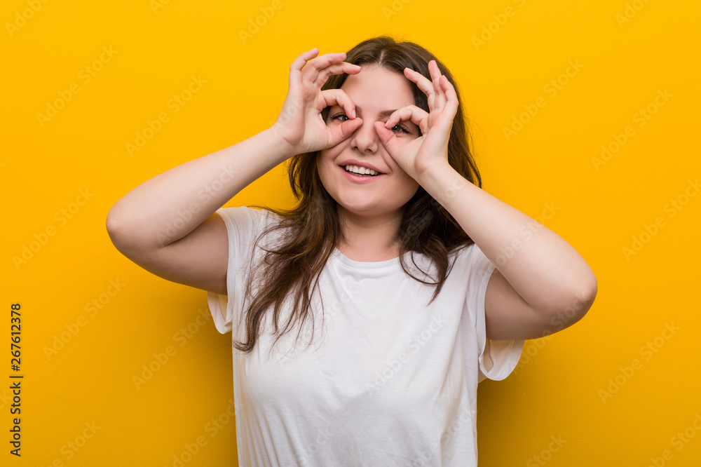 Young curvy plus size woman showing okay sign over eyes Young curvy plus size woman showing okay sign over eyes