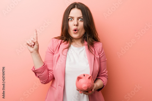 Young plus size curvy business woman holding a piggy bank having some great idea, concept of creativity.