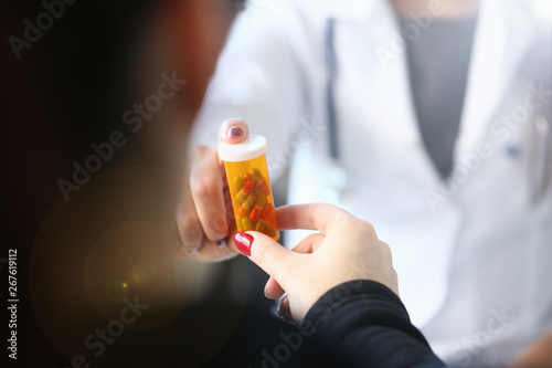 Female medicine doctor hand hold jar of pills and write prescription to patient at worktable. Panacea and life save prescribing treatment legal drug store concept.