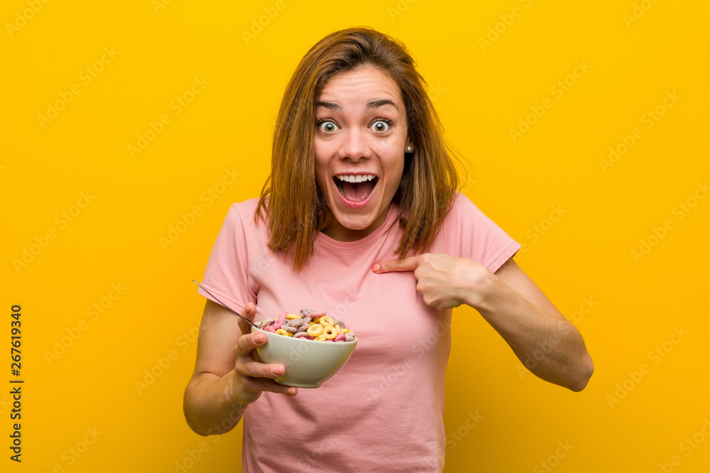 Young woman holding a cereals bowl surprised pointing at herself, smiling broadly. Young woman holding a cereals bowl surprised pointing at herself, smiling broadly.