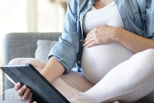 Pregnant woman using digital tablet, relaxing in couch