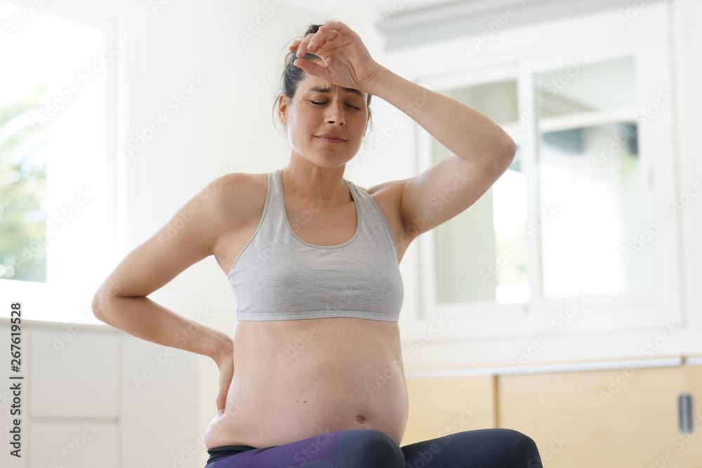 Pregnant woman at home sitting on fitness ball, doing relaxation exercises