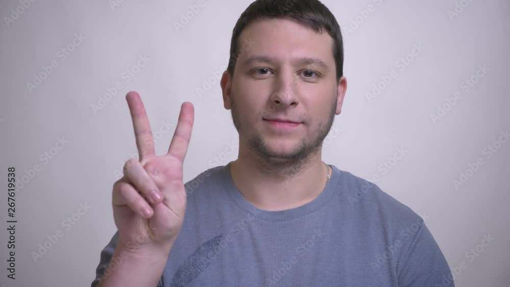 Closeup portrait of adult attractive caucasian man showing two fingers sign and smiling looking at camera with background isolated on white Closeup portrait of adult attractive caucasian man showing two fingers sign and smiling looking at camera with background isolated on white