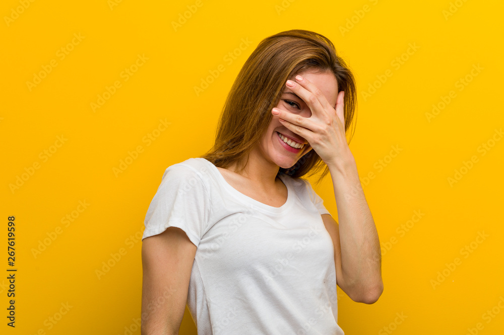 Young natural caucasian woman blink at the camera through her fingers, embarrassed covering her face.