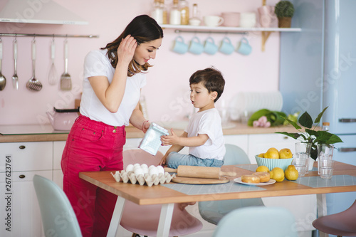 Beautiful young mother cooking with her son in kitchen at home