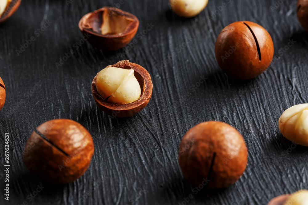 Obraz premium Purified and shell repeats macadamia nuts on black textural stone background. Healthy eating concept