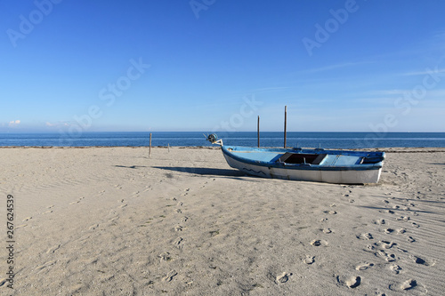 Old fishing boat left on the empty wide sandy beach, quiet afternoon on Katerini Beach, Greece photo