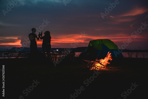 Silhouette group of Asian friends tourist drinking and playing guitar together with happiness in Summer while having camping near lake