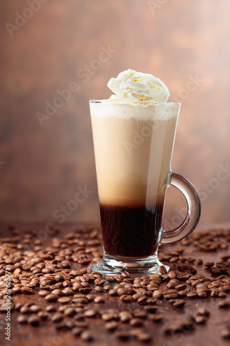 Glass cup with coffee and coffee beans on a brown background.